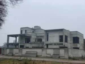 This image depicts a modern house under construction, showcasing the early stages of a residential building project. The concrete structure features a multi-level design with large window openings, indicative of contemporary architectural trends.