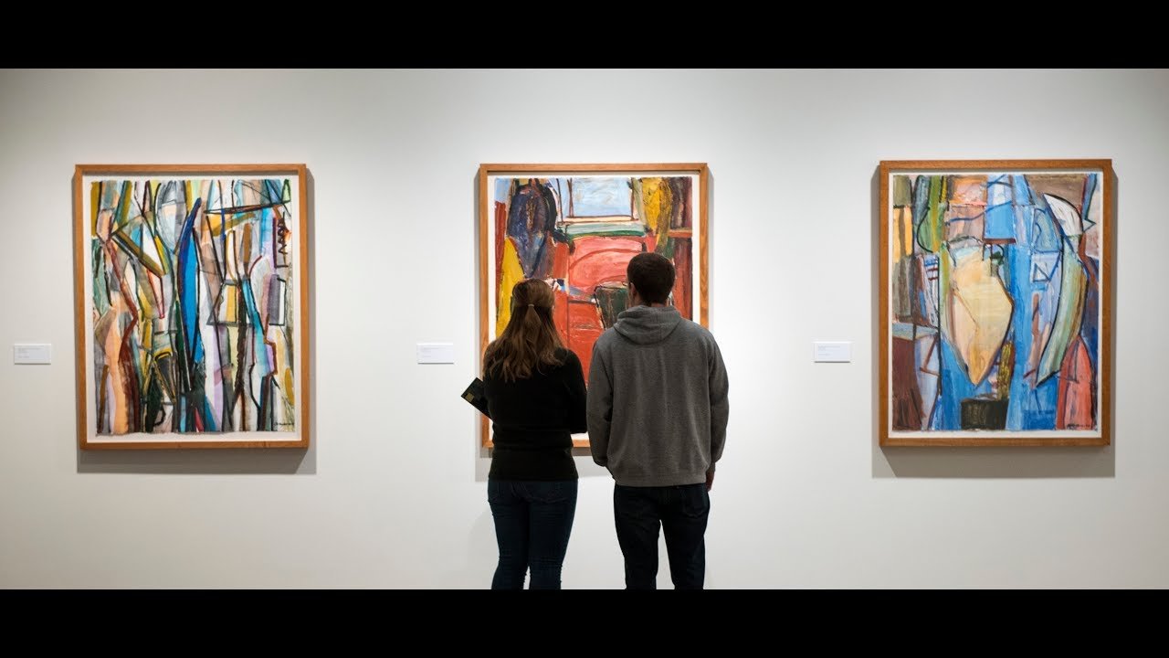 A couple observes abstract paintings in a modern art exhibition, representing the immersive experiences available at Art Galleries Near Me.